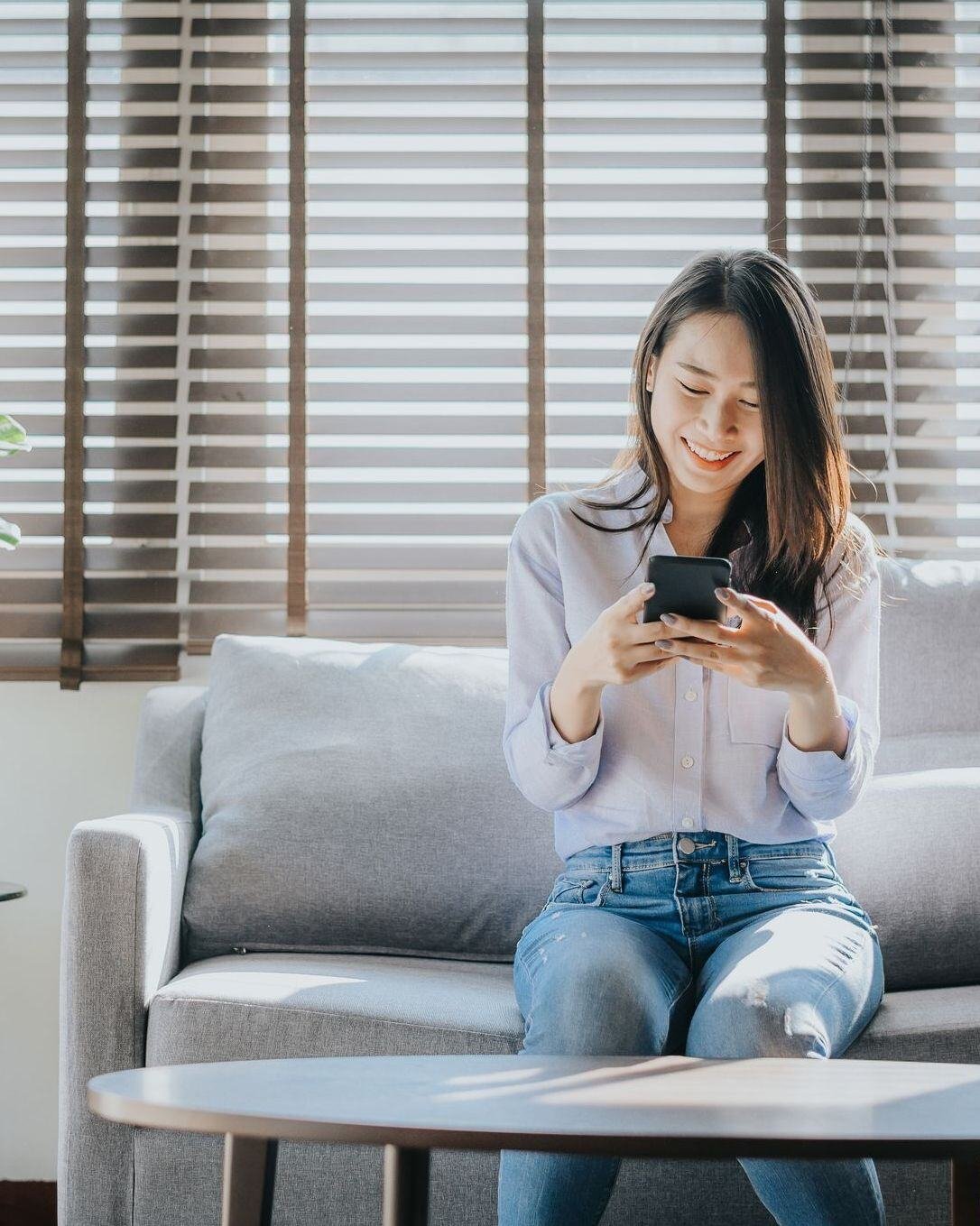 woman sitting on couch looking down at her phone.