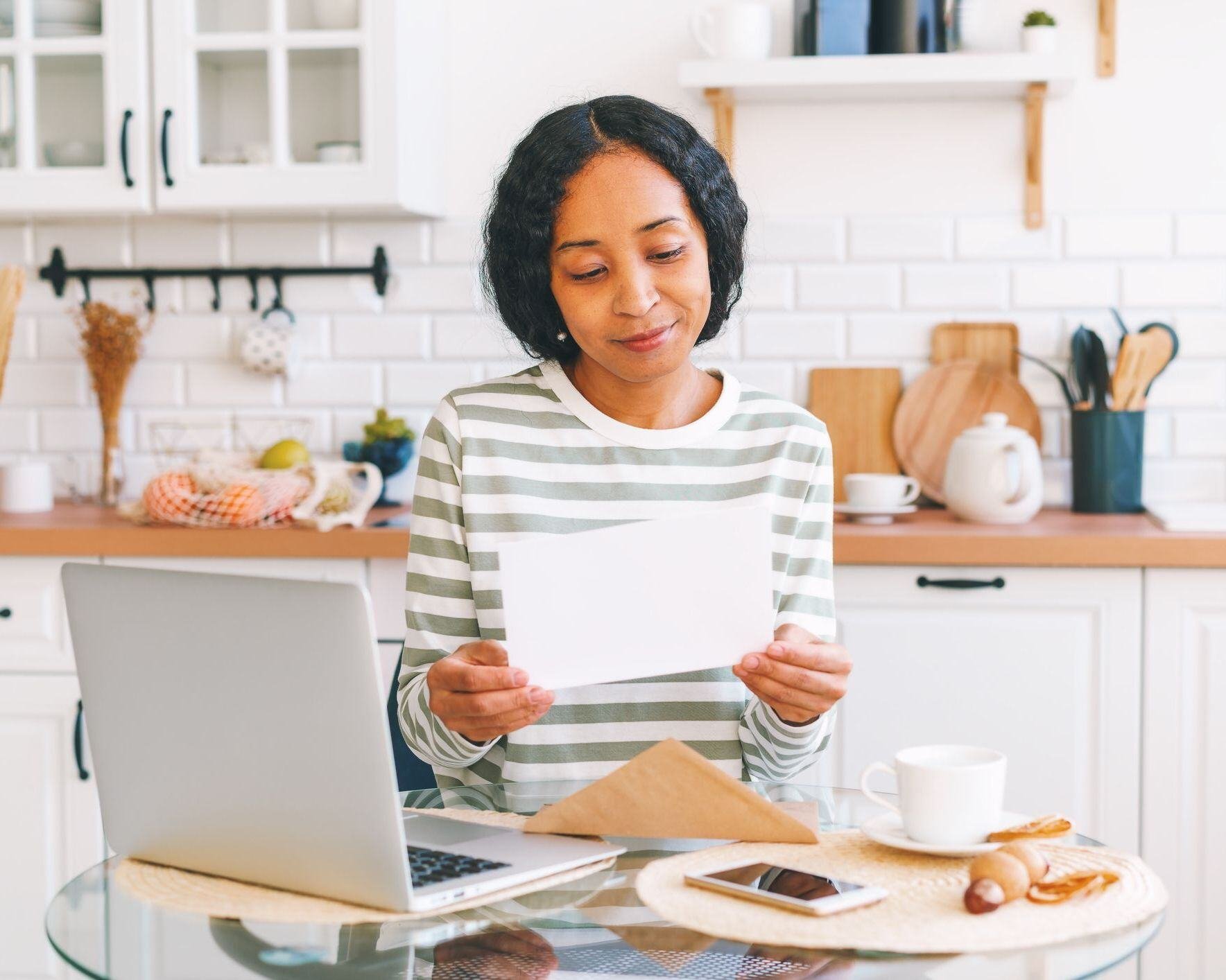 Woman reading postcard at her kitchen table.