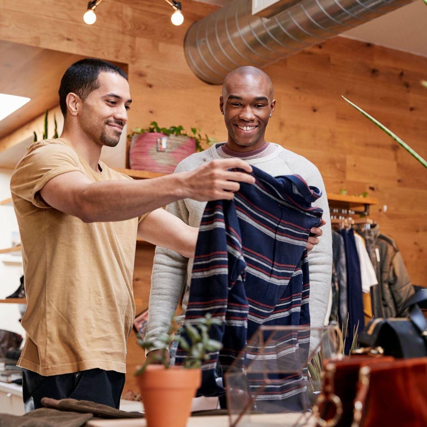Man holding clothing up showing another man.